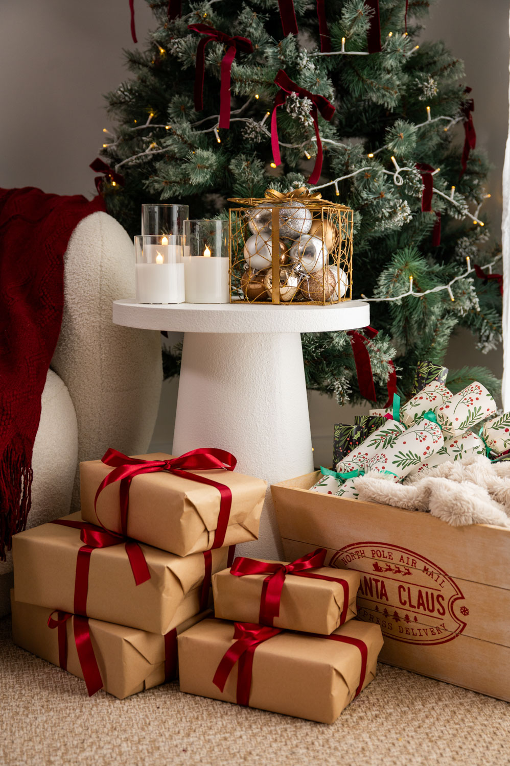 Candles, gold baubles and gifts wrapped in brown paper with red ribbons under the Christmas tree