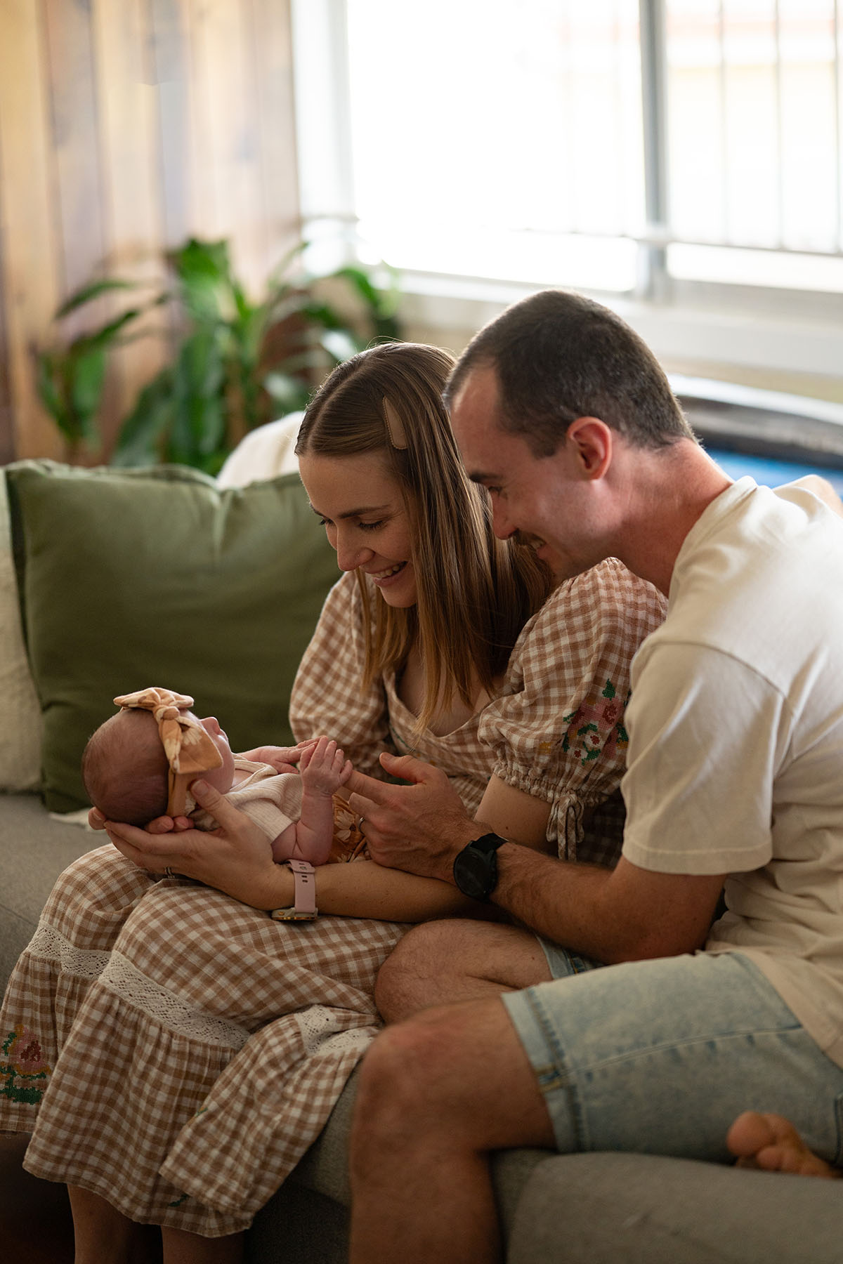 A mother and father smiling together on the couch as they admire their newborn baby