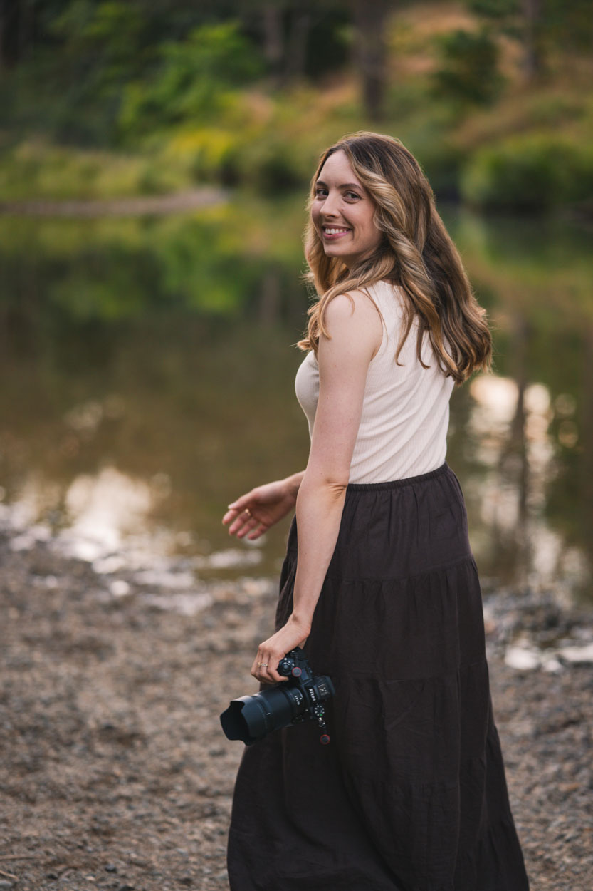 Katie standing by a still pond at golden hour with her camera