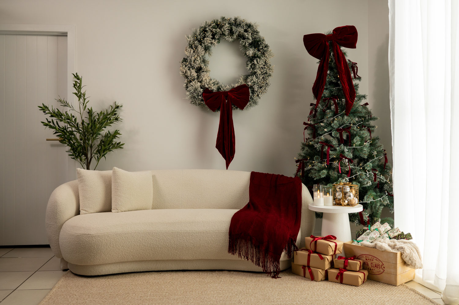 Cream couch with a red throw, frosted wreath with a red velvet bow and a decorated Christmas tree in the studio