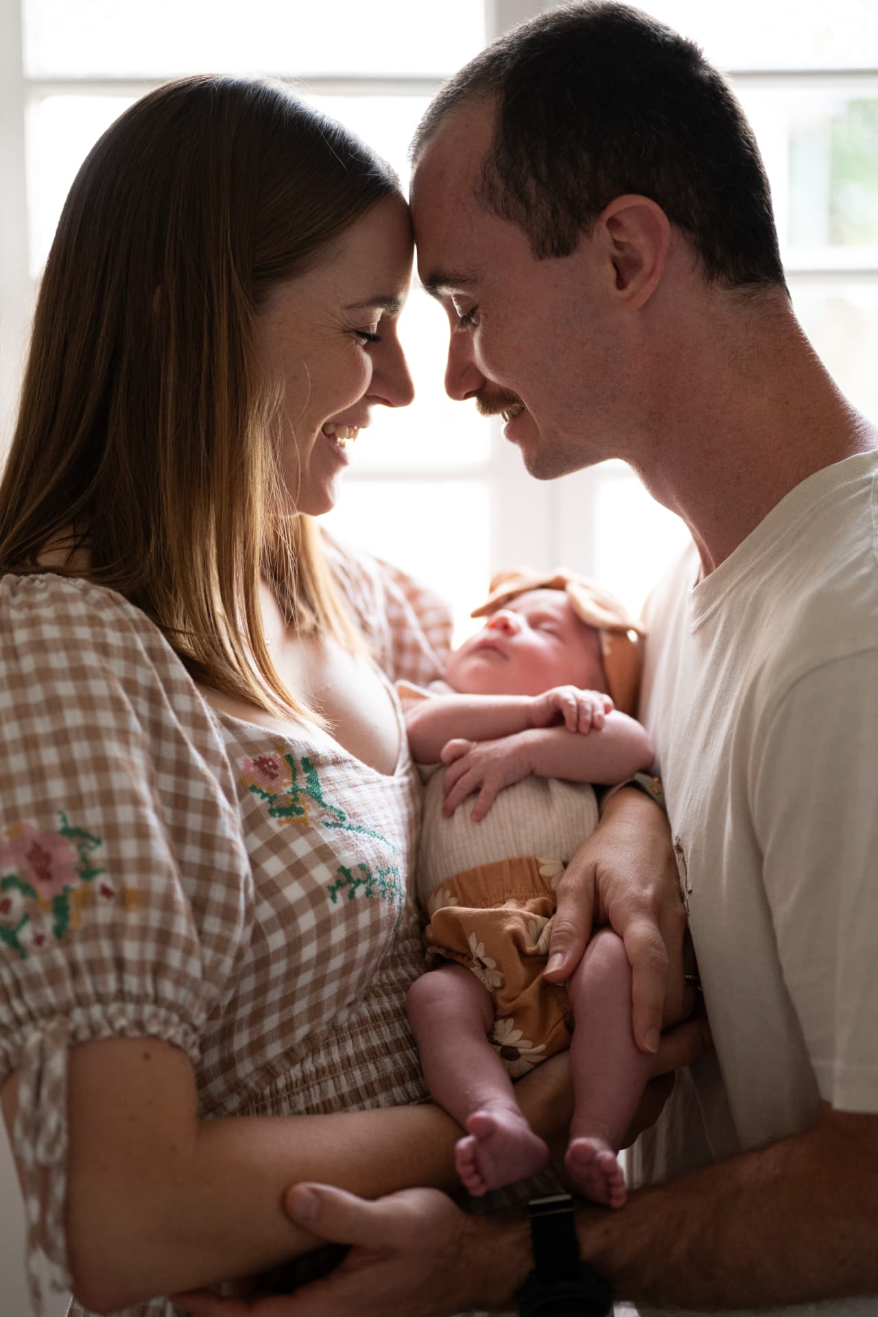 A mother and father smiling together as they hold their newborn baby